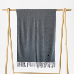 Detail view of a medium grey cashmere scarf with elegant fringe and a black woven label