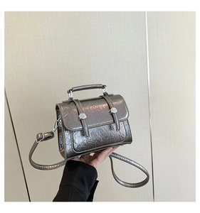 Detail of metallic silver messenger bag featuring crinkled texture and silver metal handle