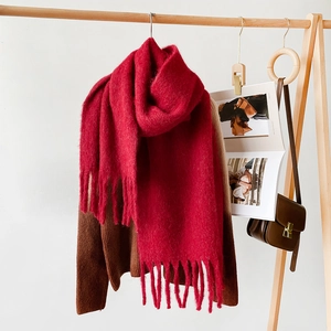 Detail of soft deep red mohair scarf with thick long tassels on a wooden hanger