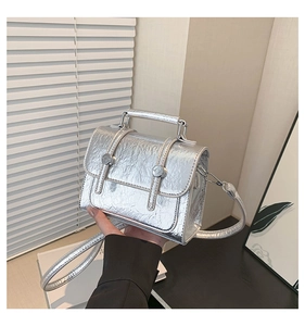 Detail of silver messenger bag with crackle texture finish and metal cylindrical buckles