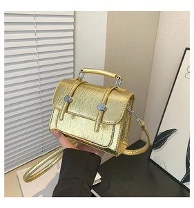 Close-up of gold metallic messenger bag with crinkled texture and dual ring lock detail