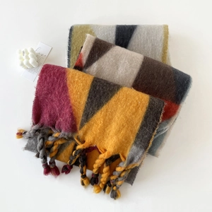Detail van zachte mohair sjaal met geometrische kleurvlakken en dikke gebreide kwastjes