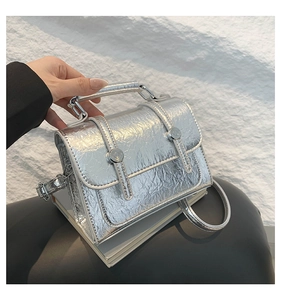 Close-up of silver messenger bag with crackle texture and metallic circular buckles