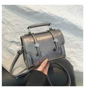 Close-up of metallic silver messenger bag with crinkle texture and round metal buckle
