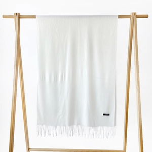 Detail of soft white cashmere scarf with fringe trim and material label on wooden hanger