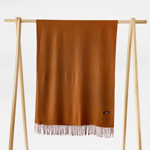 Detail of caramel cashmere scarf with fringes hanging on a wooden hanger on white background