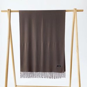 Detailed view of coffee brown cashmere scarf with fringe and label on wooden hanger