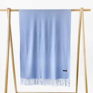 Detailed texture of light blue cashmere scarf with fine fringe on a wooden hanger