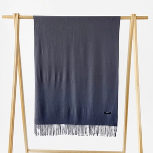 Detailed view of dark grey cashmere scarf with elegant tassels on a wooden hanger