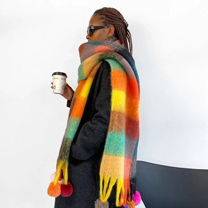 Detail view of colorful plaid winter scarf featuring vibrant pom-poms and long tassels