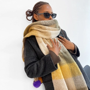 Detailed texture of thick plaid winter shawl with decorative purple pom-pom accent