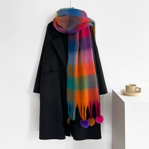 Detailed view of colorful rainbow plaid scarf with vibrant pompom tassels on black coat