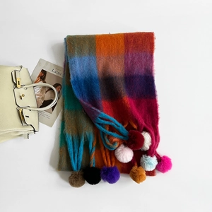 Detailed view of long thick winter scarf with colorful plaid patterns and fuzzy pom-poms