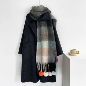 Detail of grey wool coat with colorful plaid scarf featuring vibrant handmade pom-pom charms