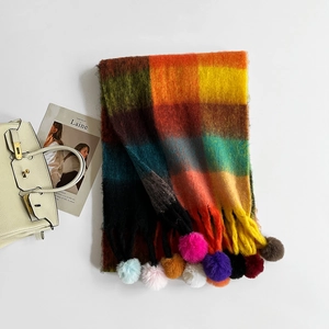 Detailed close-up of rainbow plaid knit scarf featuring vibrant pompom fringe texture