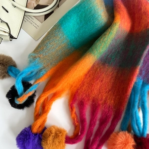 Detail view of rainbow plaid scarf featuring colorful faux fur pom-pom fringe and brushed texture