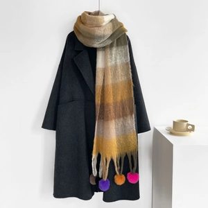 Close-up of earth tone plaid scarf with colorful pom-pom details on wool coat