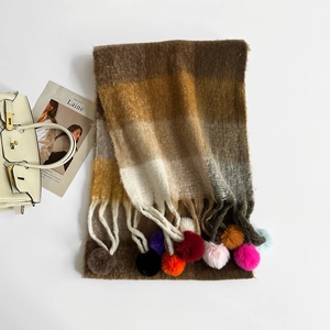 Detail shot of a knit plaid scarf with colorful pom-poms and tassels on a white background