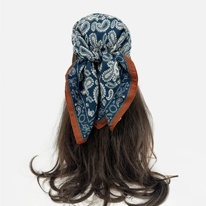Detail of navy blue paisley silk scarf tied as a headband with contrast red borders