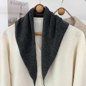 Gros plan d'une écharpe en tricot gris foncé associée à un gilet ivoire sur un cintre