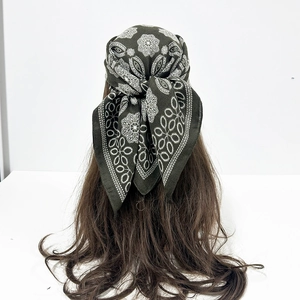 Rear view of a dark green paisley patterned silk scarf tied on long wavy brown hair
