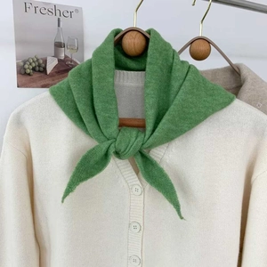 Détail d'un foulard triangle en tricot vert sur un cardigan crème montrant la texture