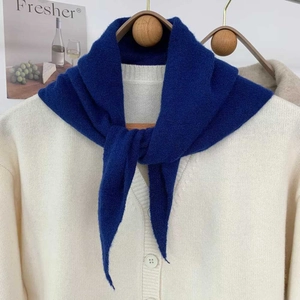 Gros plan d'une écharpe en maille bleue sur un cardigan blanc cassé sur un cintre