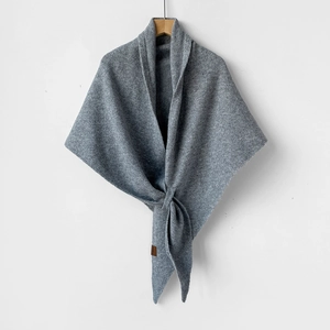 Detail of grey knitted wool shawl showing the thick fabric texture and leather logo tag