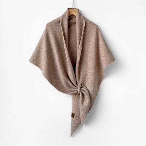 Close-up of warm camel wool knit shawl with asymmetric knot design and leather tag detail