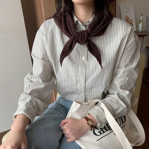 Détail d'un foulard triangulaire en tricot marron foncé avec chemise à rayures et sac