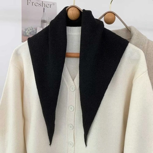 Vue détaillée d'une écharpe triangle en tricot noir sur cintre avec cardigan blanc