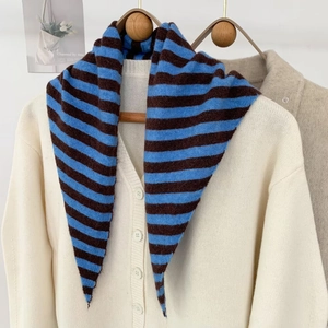 Détail du châle en laine à rayures bleues et marron sur un cardigan beige clair