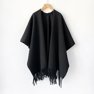 Detalle de chal negro tipo cachemira con flecos de borlas en una percha de madera