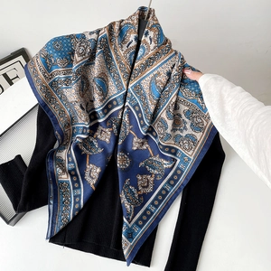 Close-up of a blue paisley silk scarf draped on a black sweater showing premium texture