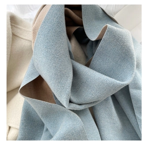 Texture détaillée de l'écharpe en cachemire réversible bleu clair et camel sur manteau