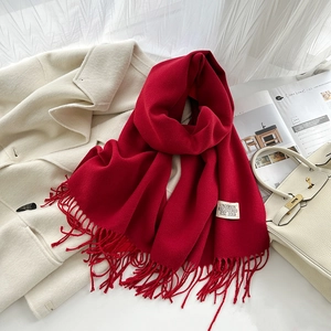 Détail de l'écharpe rouge aspect cachemire avec franges et étiquette sur manteau