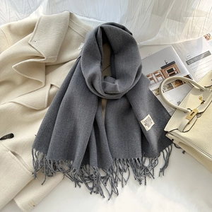 Détail d'une écharpe gris foncé avec étiquette tissée blanche et bords à franges