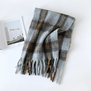 Flat lay of a thick taupe checkered wool scarf with fringes and a fashion magazine