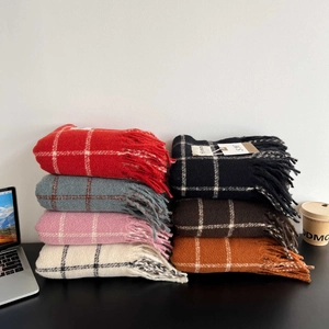 Detail view of multi-color plaid scarves with fringe on a cozy winter desk setup