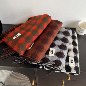 Close-up of four thick plaid scarves with tassels and labels on a wooden table