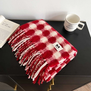 Detail of red and white plaid cashmere-feel scarf featuring tassels and a woven logo label