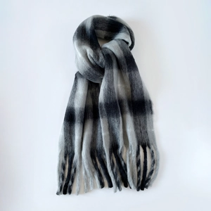 Close-up of fluffy mohair scarf with black and grey plaid pattern and long tassel details