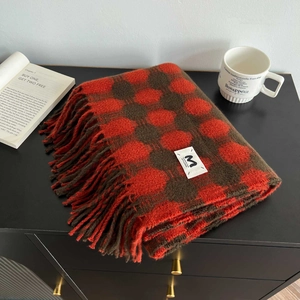 Detail of red-brown checkered scarf with soft fringes and brand label on a cozy wooden table