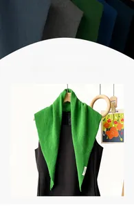 Detail of green knitted wool triangle scarf draped over a black dress with visible texture