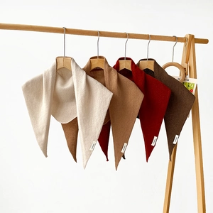 Close-up of wool triangular scarves in beige, camel, red and coffee on wooden hangers