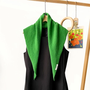 Close-up of a green 100% wool knit triangle scarf with a detailed composition label