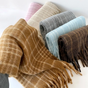Detail showing various colors of plaid wool scarves with long tassels and fuzzy texture