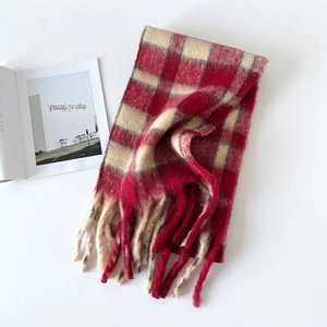 Détail d'une écharpe en laine à carreaux rouge et beige avec des pompons doux