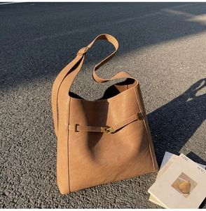 Close-up of tan leather bucket bag with gold metal buckle on sunlit street