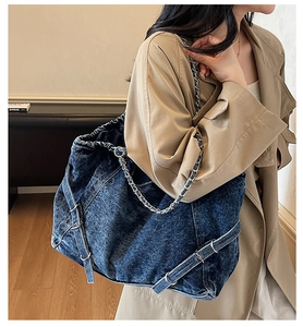 Detail of deep blue denim tote bag featuring metallic chain strap and side buckle adjustment